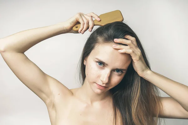 Joven hermosa chica peinando su largo cabello rubio con un peine de madera —  Fotos de Stock