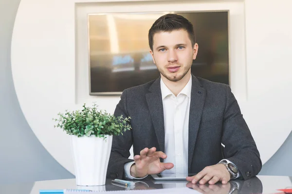 Young successful man in suit sitting at desk in office — Stock Photo, Image