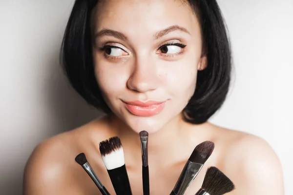 Όμορφο κορίτσι, με μαύρα μαλλιά κρατώντας ένα πινέλο για το make up. η γυναίκα μοιάζει μυστηριωδώς στην άκρη — Φωτογραφία Αρχείου