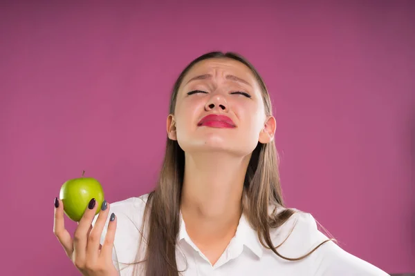 Encantadora chica con los ojos cerrados y una cara disgustada sosteniendo una manzana en sus manos — Foto de Stock