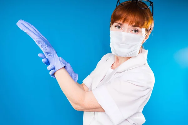 En kvinna i medicinska kläder och glasögon sätter på handskar och ser på kameran — Stockfoto