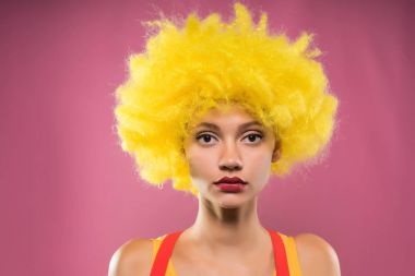 doğrudan kameraya, pembe bir arka plan üzerinde izole sarı peruk içinde ciddi kız görünüyor