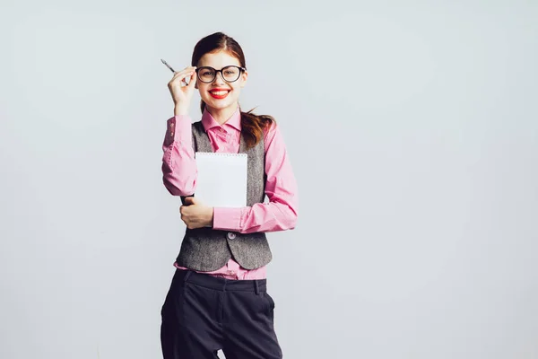 Ein nettes Mädchen mit Brille und rotem Lippenstift hält Papierblätter und Bleistift in den Händen. Mädchen hält Brille in der Hand und blickt in die Kamera — Stockfoto