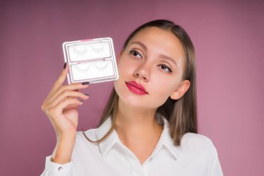 Güzel bir kız güzel büyük dudaklar ile sahte kirpik tutuyor. Bir pembe izole.