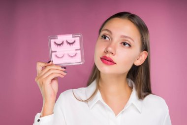 Güzel bir kız güzel büyük dudaklar ile sahte kirpik tutuyor. Bir pembe izole.