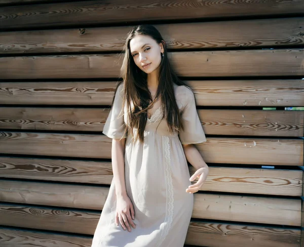 Uma senhora com cabelos longos em um lindo vestido bege olha para a câmera, em um fundo de madeira . — Fotografia de Stock