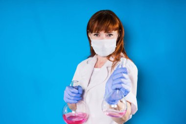 bir kadın Beyaz önlük, tıbbi maske ve eldiven kimyasal deneyler yapıyor. Mavi bir arka plan üzerinde izole
