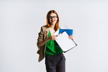 Kızıl saçlı kız gözlük ve kırmızı dudaklar ile bir klasör ile kağıtları, gülümseyen ve kameraya bakıyor tutuyor. izole