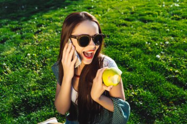 Konuşan kadın elbiseli, güneş gözlüğü çimenlerin üzerinde oturan hareket eden, tutan