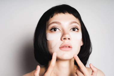 kısa siyah ve silikon yamalar gözlerinin altındaki genç bir kızla parmaklarını yüzünü gösterir.