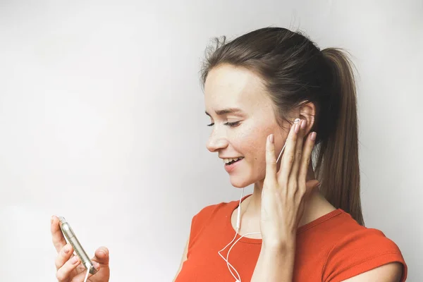 Krásná mladá dívka v červené tričko sledování videa na svém smartphonu se sluchátky — Stock fotografie