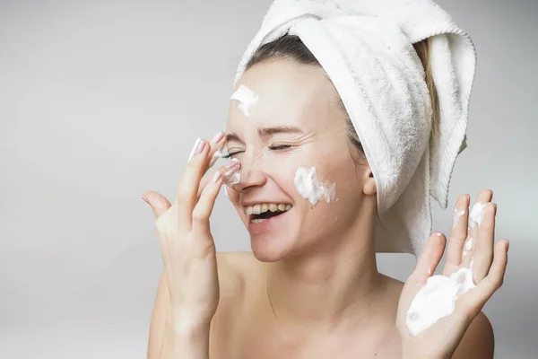 Mujer divertida en una toalla en la cabeza feliz limpia la piel con espuma sobre un fondo blanco aislado. Concepto de limpieza del cuidado de la piel —  Fotos de Stock