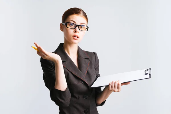 Young beautiful modern girl in glasses and a strict suit holds documents in her hands and looks surprised — Stock Photo, Image