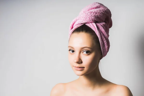 Jovem menina bonita com pele limpa e com uma toalha rosa na cabeça olhando para a câmera — Fotografia de Stock