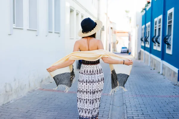 Uma jovem em um vestido bonito e longo chapéu caminha ao longo de uma rua pavimentada — Fotografia de Stock