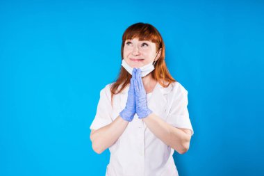 yetişkin kadın doktor koruyucu maske ve beyaz tıbbi sabahlık gülümsüyor ve katlanmış silah ile standları