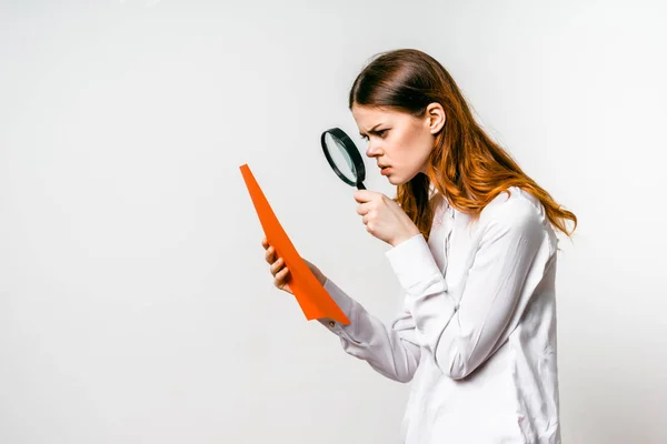 Young beautiful serious in a white shirt with a magnifying glass reading from a sheet — Stock Photo, Image