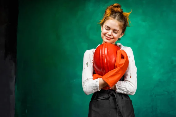 Buena chica en ropa de trabajo y guantes de goma naranja sostiene un casco en sus manos, aislado — Foto de Stock
