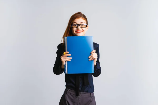 Nettes Mädchen mit roten Lippen in Brille hält einen blauen Ordner in die Kamera, isoliert auf weißem Hintergrund — Stockfoto