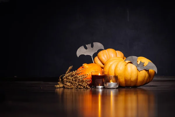 Abóbora grande de Halloween com folhas douradas de outono, grama seca, velas ardentes em um fundo preto — Fotografia de Stock