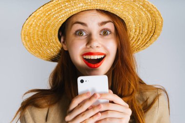 neşeli kız büyük bir şapka ve kırmızı dudaklar ile bir telefon elinde tutan ve kameraya gülüyor