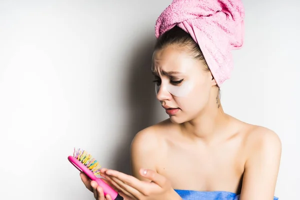 Mädchen nach der Dusche mit einem rosa Handtuch auf dem Kopf, das unzufrieden auf ihre Haarbürste blickt, isoliert — Stockfoto