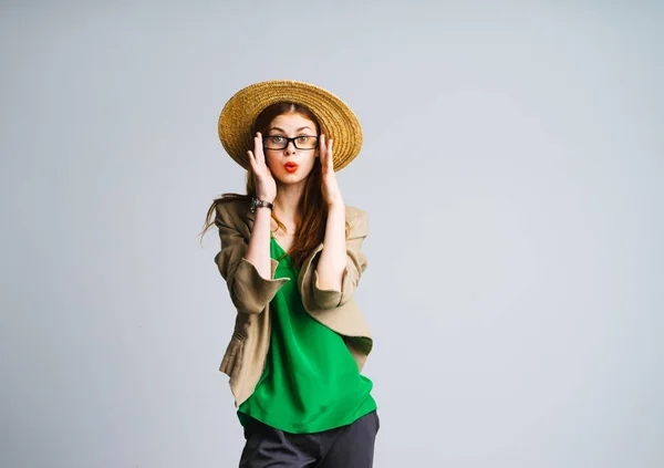 Una ragazza con le labbra rosse e in un grande cappello e occhiali guarda la fotocamera. Donna in camicetta verde brillante, isolata — Foto Stock