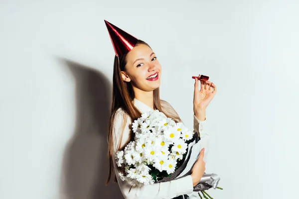 Uma jovem menina bonita celebra algo, mantém um grande buquê de flores brancas, um boné festivo na cabeça — Fotografia de Stock
