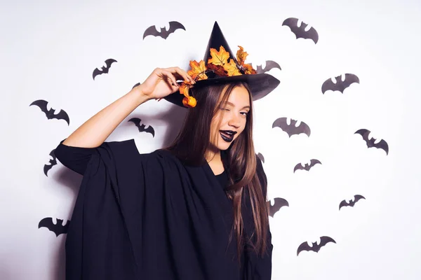 Krásné sexy gotická dívka v čarodějnice halloween, ve velkým černým kloboukem, zdobí žluté listy, mrknutí — Stock fotografie