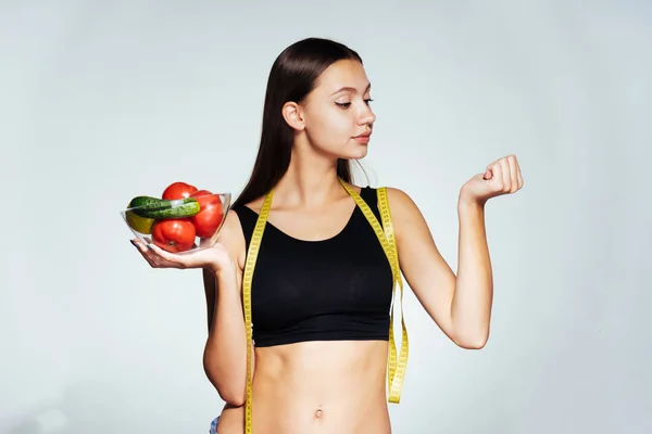 Jovem menina esportiva observa sua figura, sorri, segura um prato de vidro com vegetais úteis e frutas em suas mãos — Fotografia de Stock