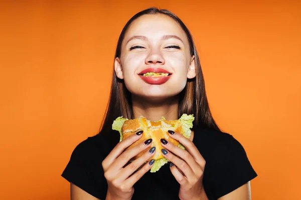 Молода щаслива дівчина хоче схуднути, але їсть нездоровий висококалорійний бургер — стокове фото