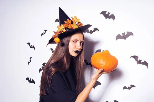 En ung sexig gotisk flicka firar halloween, klädd i en häxa, helt svarta kläder, innehar en pumpa i hennes händer — Stockfoto