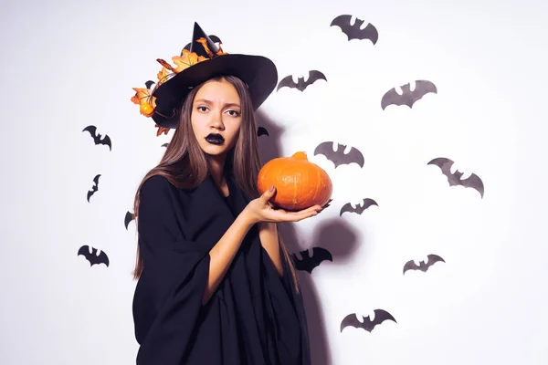 Una joven chica gótica sexy celebra Halloween, vestida con una bruja, ropa completamente negra, sostiene una calabaza en sus manos — Foto de Stock