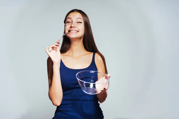 Молодая счастливая девушка в голубом топе хочет сбросить вес, держит пустую стеклянную тарелку и вилку — стоковое фото