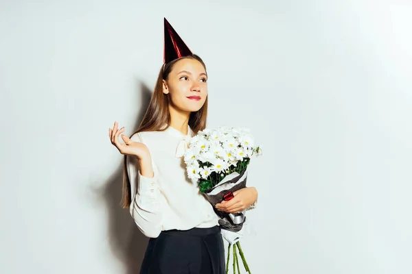 Jovem bela menina feliz celebrando algo, segurando um grande buquê de flores brancas, sorrindo, em sua cabeça um chapéu festivo vermelho — Fotografia de Stock