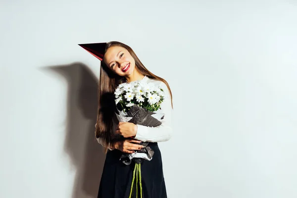 Joven hermosa chica feliz celebrando algo, sosteniendo un gran ramo de flores blancas, sonriendo, en su cabeza una gorra roja festiva — Foto de Stock