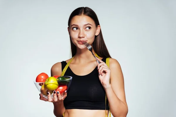Mladé krásné sportovní dívka sleduje její postavu, drží desku s užitečné zeleniny a ovoce ve svých rukou — Stock fotografie