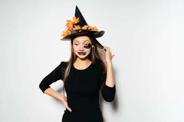 Joven chica gótica sexy celebra halloween en la imagen de una bruja, en un gran sombrero negro, se ve divertido — Foto de Stock