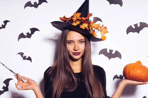 Una joven gótica sexy celebra halloween en forma de bruja, con un gran sombrero negro, sostiene una calabaza y una varita mágica en sus manos —  Fotos de Stock