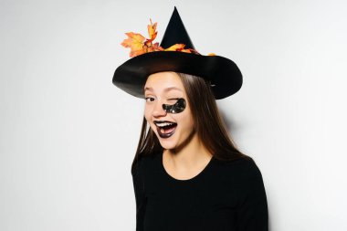 Cadılar Bayramı, cadı, büyük bir siyah şapkalı giymiş seksi Gotik kız kutluyor bir genç sarı sonbahar yaprakları, Göz kırpmalar dekore edilmiştir.