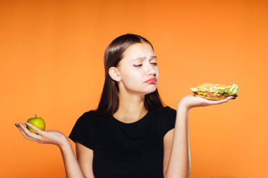 güzel kız, kilo vermek istiyor bir genç tutan onun elinde bir sağlıksız kalori hamburger ve yararlı bir elma