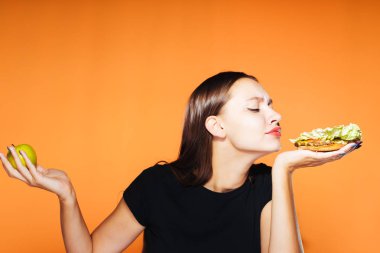 güzel bir genç kız, kilo vermek istiyor hevesle zararlı kalori hamburger yiyor ama yararlı bir elma elinde tutan