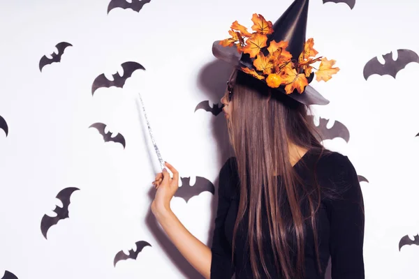 Ein junges sexy gothisches Mädchen feiert halloween, gekleidet in eine Hexe, mit einem großen schwarzen Hut verziert mit gelben Herbstblättern, hält einen Zauberstab in ihren Händen — Stockfoto