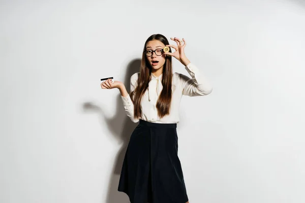 Una joven y exitosa chica moderna con gafas lleva en sus manos una bicoína dorada y una tarjeta bancaria — Foto de Stock
