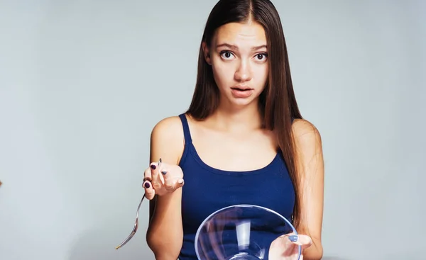 A young athletic girl in a blue top watches her figure, holds an empty glass plate and a fork — Stock Photo, Image