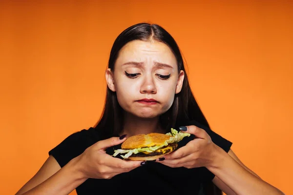 Krásná mladá dívka chce zhubnout, ale dychtivě jí škodlivé vysokokalorickou burger — Stock fotografie
