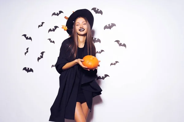 Ein junges sexy Gothic Girl feiert Halloween, in eine Hexe gekleidet, hält einen Kürbis in ihren Händen — Stockfoto