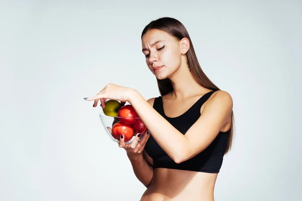 Uma jovem atlética em um top preto mantém o controle de sua figura, segura um prato com vegetais úteis e frutas em suas mãos — Fotografia de Stock