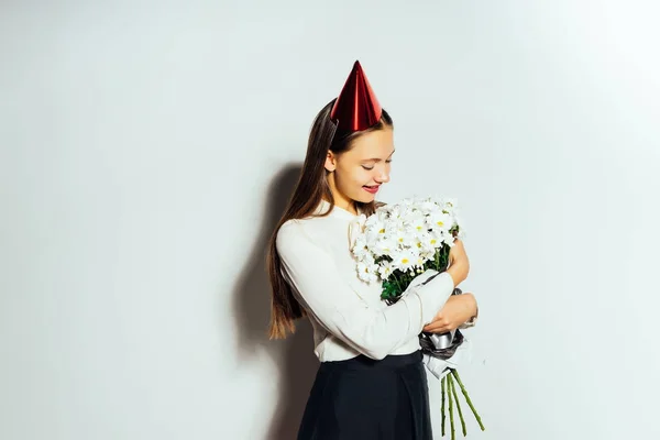 Ung vacker flicka firar något, på huvudet en röd mössa, innehar en stor bukett av vita blommor — Stockfoto