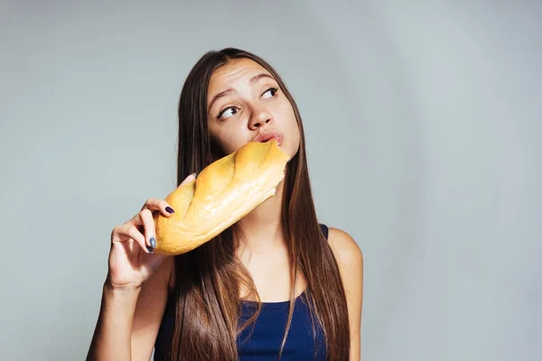 Ein junges schönes Mädchen in blauem Oberteil will abnehmen, isst aber eifrig ungesundes Weißbrot — Stockfoto